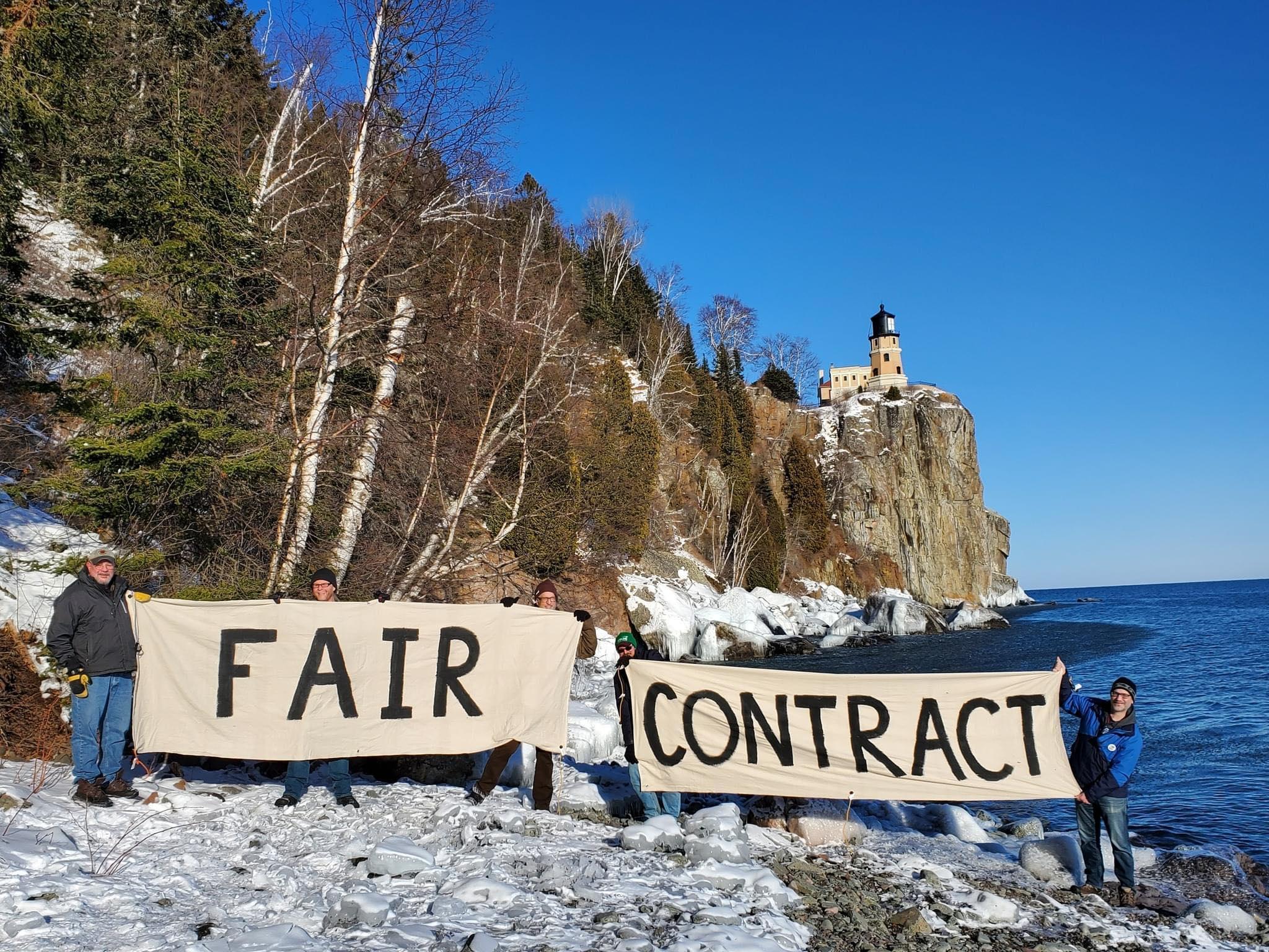 Picture of people holding a sign reading "fair contract" in front of Split Rock Lighthouse.